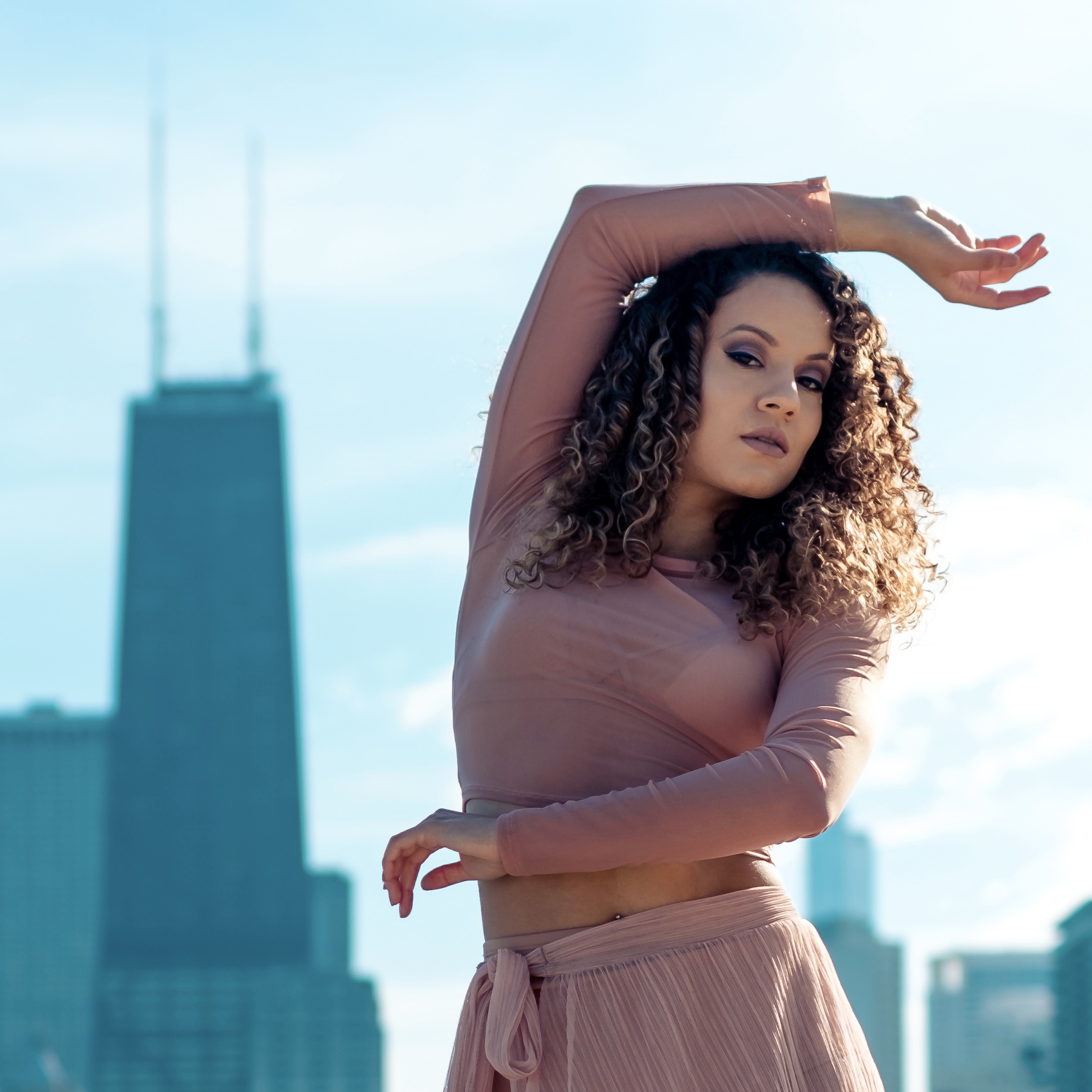 A dancer poses outdoors under a blue sky with skyscrapers in the background.